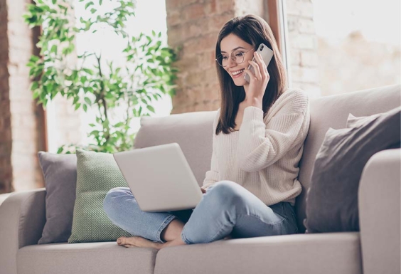 femme assise sur le canapé au téléphone avec un ordinateur sur les genoux